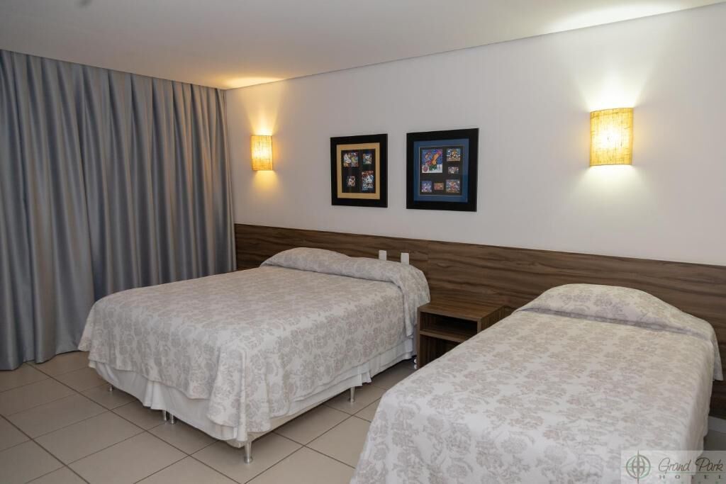 Una habitación de hotel con dos camas, cabecero de madera, lámpara de pared e imágenes enmarcadas.