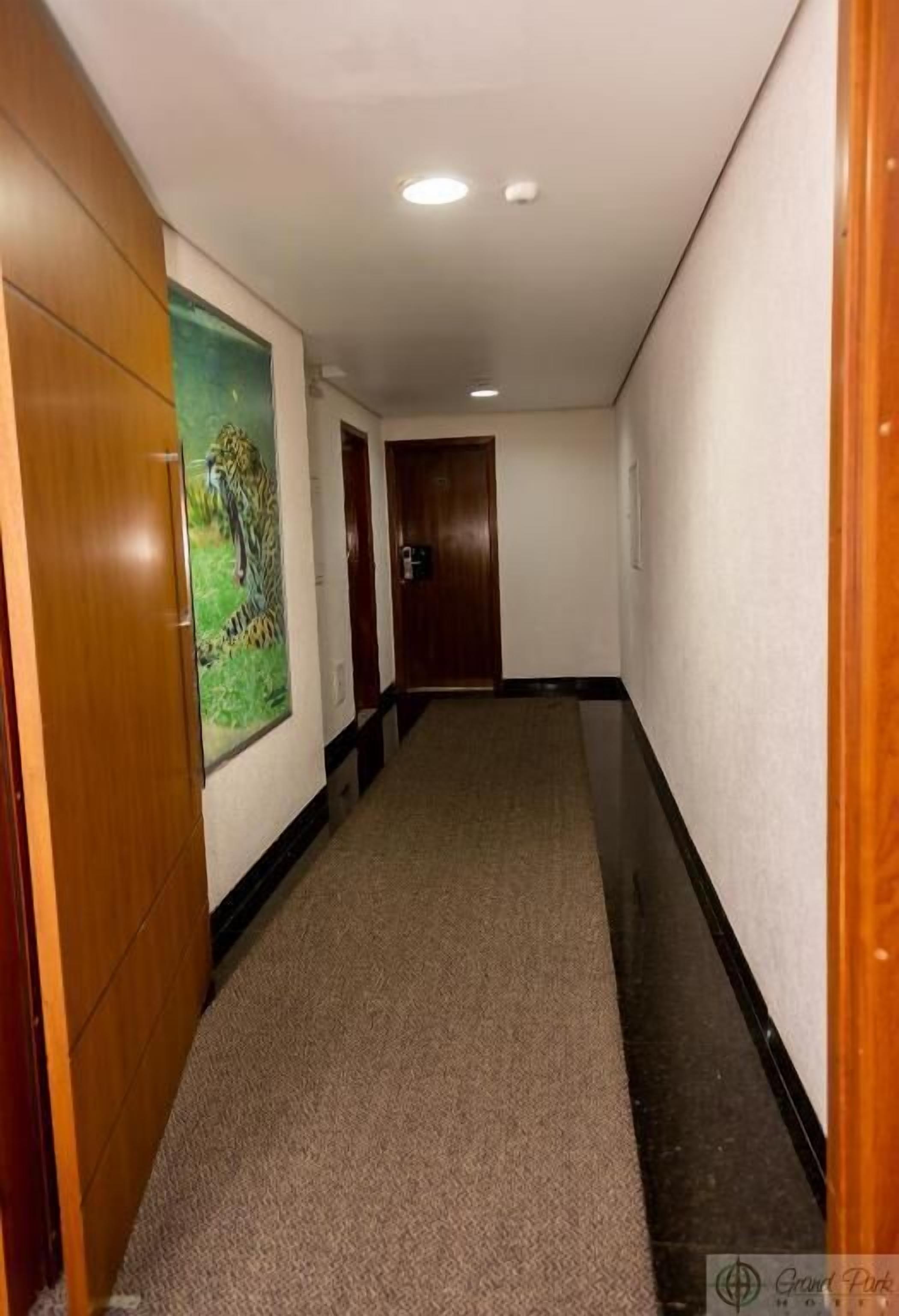 A hallway with a carpeted floor, wooden doors, and a painting on the wall.