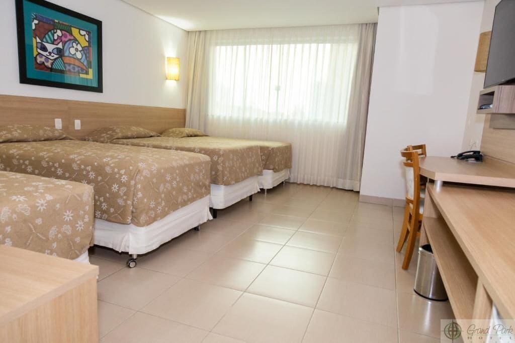 Una habitación de hotel con tres camas, un escritorio, una silla y una televisión.