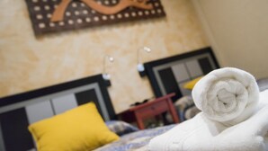 A neatly made bed with a rolled white towel, a yellow pillow, and a decorative wall piece above the bed.