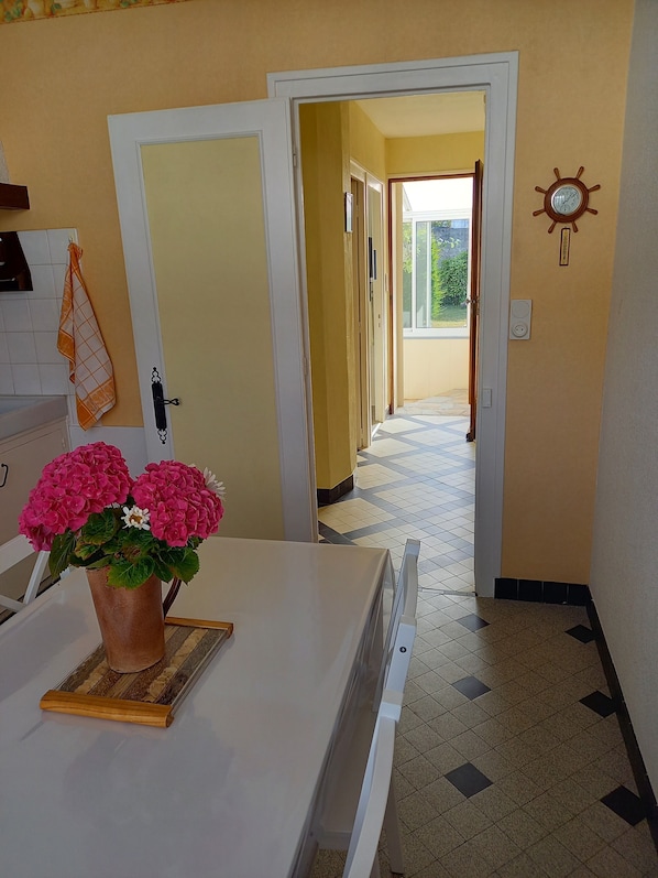 A hallway with a white door, a potted plant with pink flowers, and a clock on the wall.