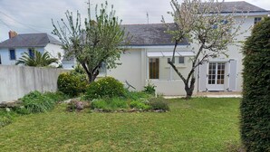 Propiedad residencial con césped cuidado, diversas plantas florecientes y una casa de techado de tejas y fachada blanca.
