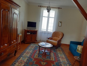Een woonkamer met een houten kast, een televisie op een standaard, een kamerkleed met patroon, een leren fauteuil en een blauwe bank.