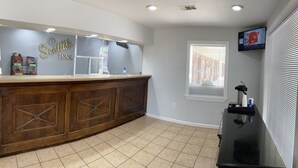 A bar area with a wooden counter, a clock, and a window with blinds. - Scottish Inns Jonesboro AR  (Jonesboro)