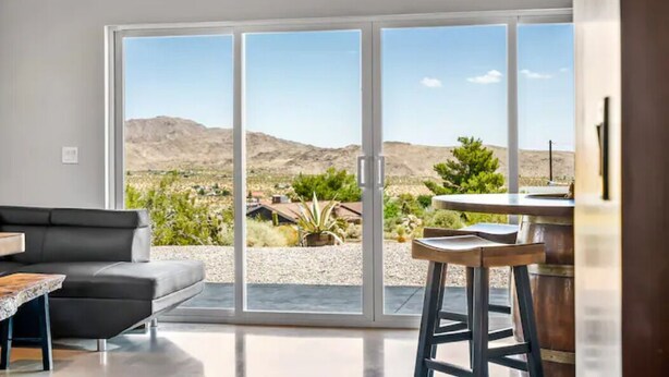 A modern living room with a large sliding glass door leading to a patio with a view of a desert landscape.