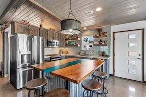 A modern kitchen with stainless steel appliances, a wooden island, and bar stools. - Luxurious STUDIO 19 - Quiet - Views  - Town in 5 mins - JTNP - in  8 minutes (Joshua Tree)