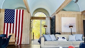 A living room with a large American flag, a sofa, a coffee table, and a view through a large arched window.
