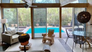 A spacious living room with a large glass door leading to a pool, wooden furniture, and a view of the outdoors.