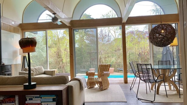 A spacious living room with a large glass door leading to a pool, wooden furniture, and a ceiling fan.