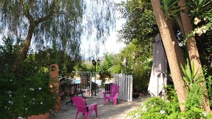 A patio area with two pink chairs, a white fence, and a tree with hanging branches. - Locations de Vacances (Porticcio)