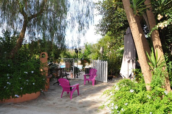 A patio area with two pink chairs, a white fence, and a tree with hanging branches. - Locations de Vacances (Porticcio)