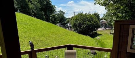 Une terrasse en bois, aménagée avec du mobilier d’extérieur, notamment une table ronde et des chaises, qui offre une vue sur une colline verdoyante.