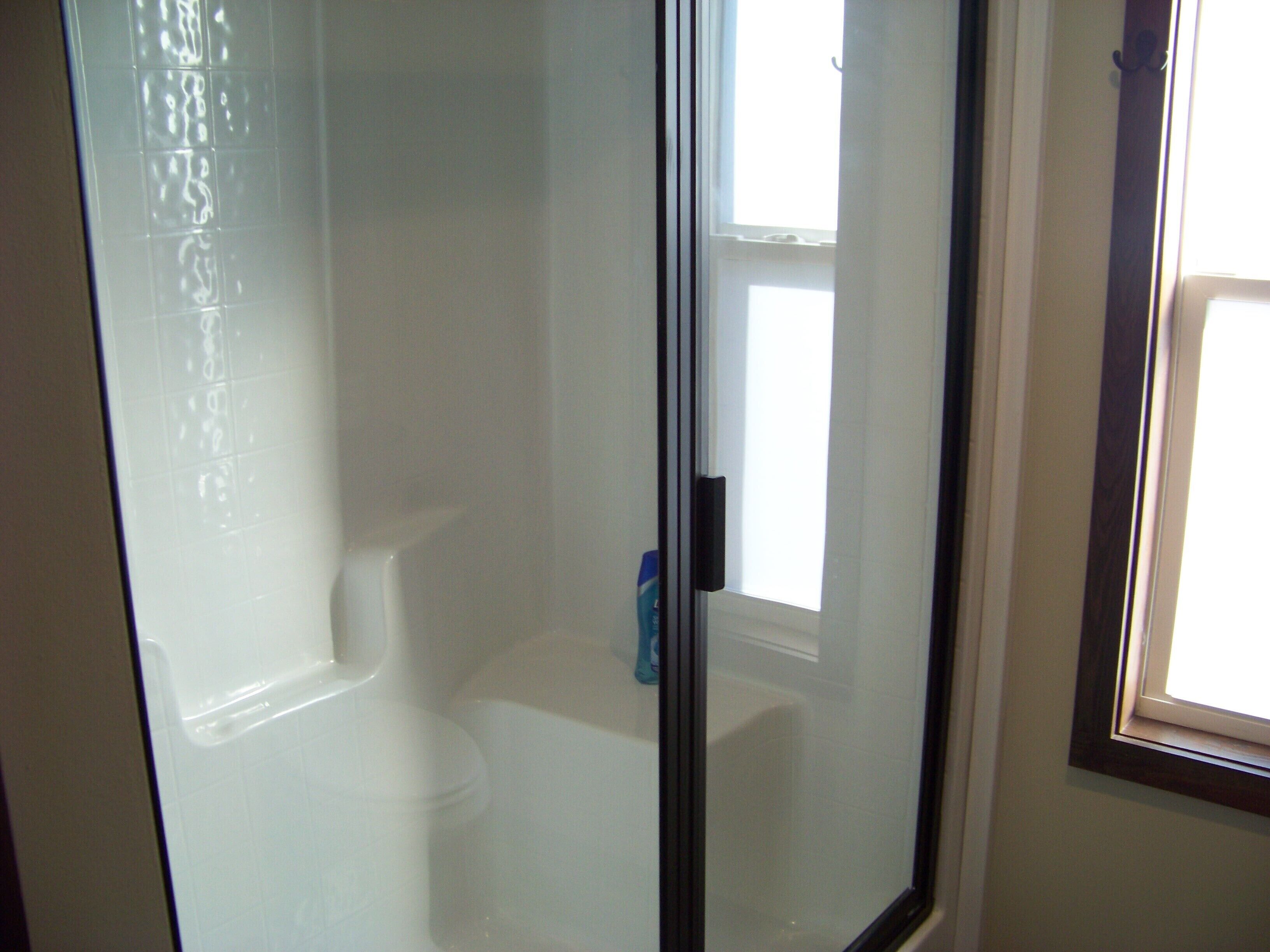 A bathroom with a glass shower enclosure, a toilet, and a window.