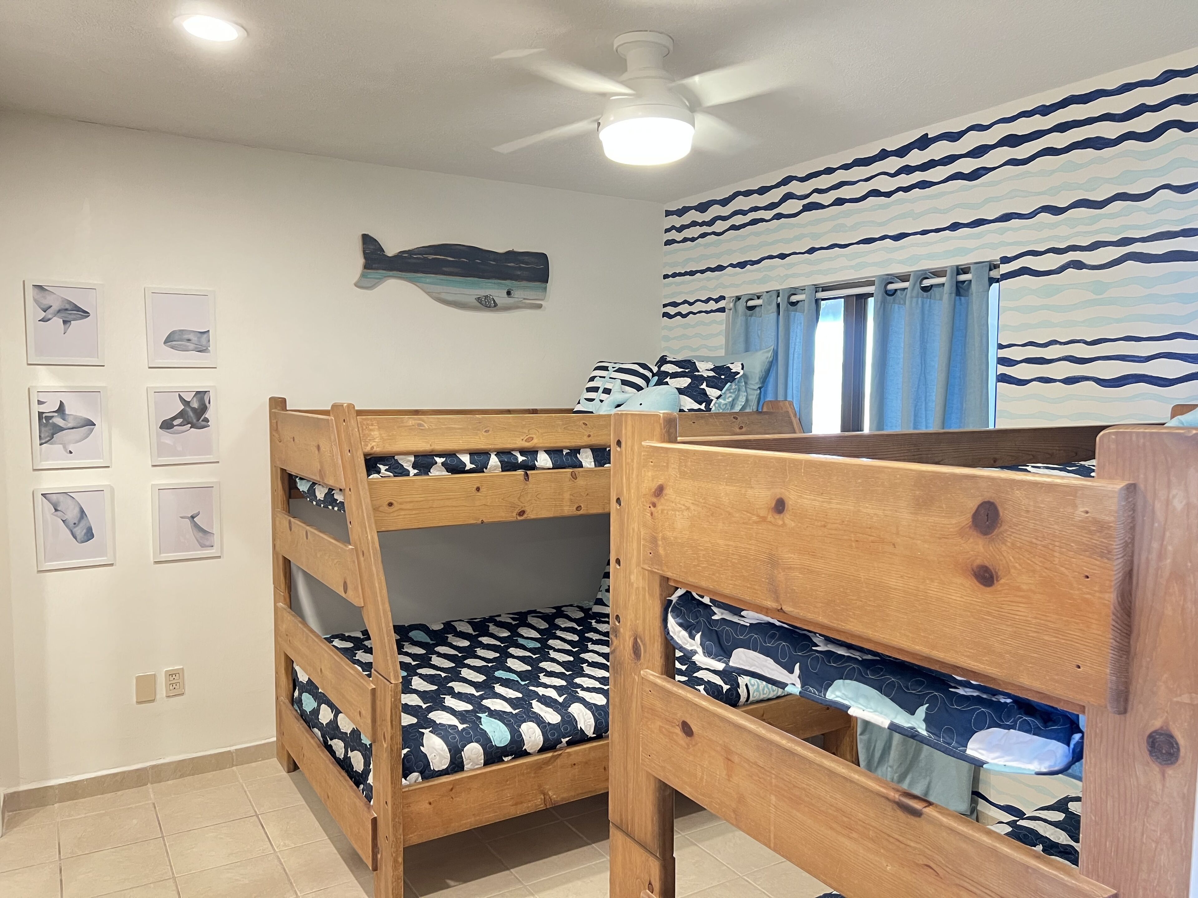 A bunk bed room with a ceiling fan, a wall with whale illustrations, and a patterned curtain.