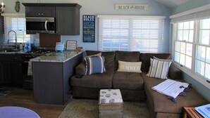Eine Küche mit Kochinsel, ein Essbereich mit braunem Sofa und Kissen, und ein Schild mit der Aufschrift 'BEACH HOUSE'.