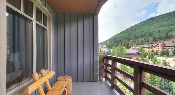 Enjoy breathtaking views of the surrounding mountains from this balcony, featuring a comfortable bench and a small table.