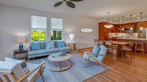 A modern living room with a sofa, coffee table, and chairs, a dining area with a table and chairs, and a kitchen with wooden cabinets and stainless steel appliances. - Luxury 3BR Poipu Paradise: Pool, Hot Tub, Gym, AC, Golf Course (Koloa)