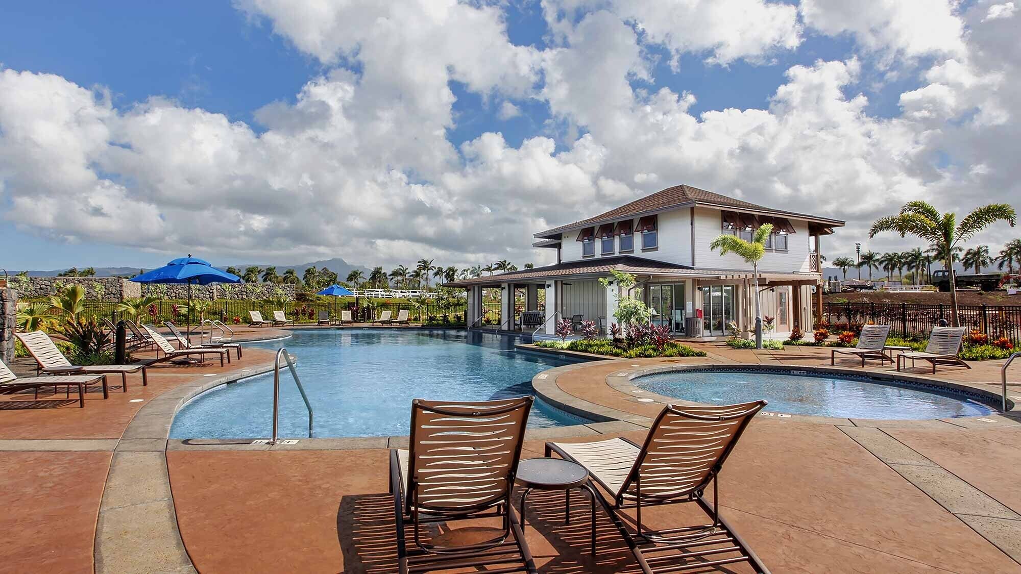 A resort pool area with lounge chairs, a two-story building, and a view of mountains.