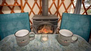 Une pièce chaleureuse avec une cheminée, deux tasses sur une table et une bougie.