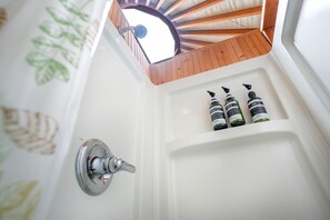 A bathroom with a wooden ceiling, a showerhead, and three bottles of toiletries on the sink.