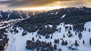 Paisaje montañoso cubierto de nieve con pistas de esquí y un edificio pequeño, probablemente una cabaña o local de alquiler de esquíes.