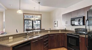 Enjoy cooking in this well-equipped kitchen with a granite countertop, dark cabinetry, and stainless steel sink.