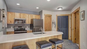Kitchen area with central island, sink, and stools, featuring a refrigerator, microwave, and oven.