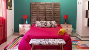 Un dormitorio con una cama grande, dos mesitas de noche, un banco y una alfombra colorida a rayas.