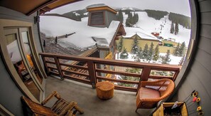 Enjoy breathtaking views of the snow-covered landscape from this balcony, featuring a wicker chair and a small stool.