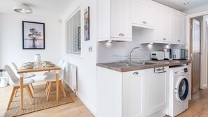 Ett kompakt kök med vita skåp, en inbyggd tvättmaskin och en matplats med bord och stolar.