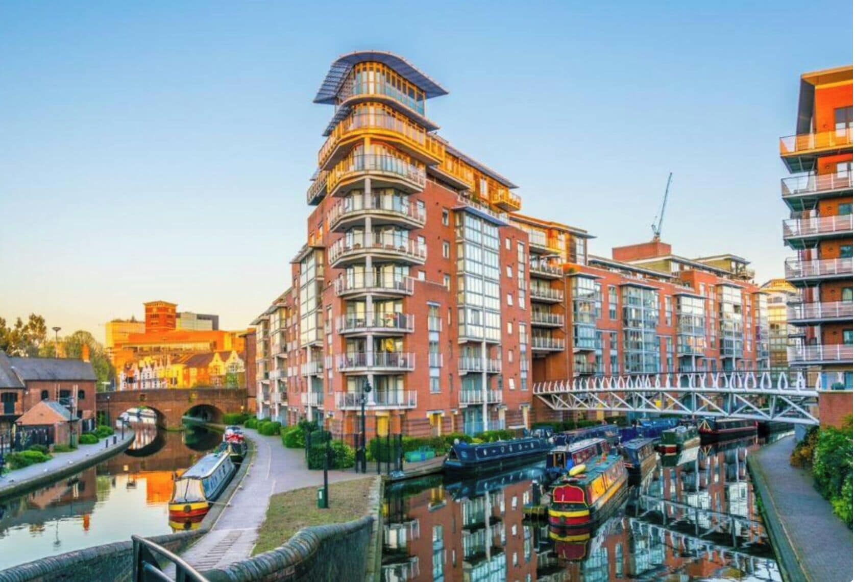 A modern multi-story building with balconies, a canal, and a bridge.