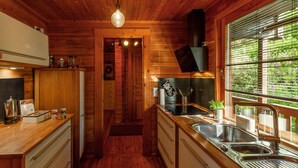A wooden cabin interior with a kitchen area, wooden cabinets, a sink, and a window with blinds.