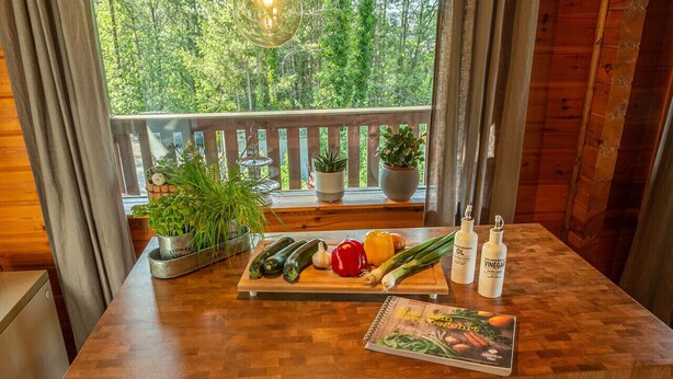 A wooden table with fresh vegetables, a cookbook, and cooking oil bottles.