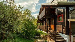 A rustic wooden house with a balcony, a stone pathway, and lush greenery.