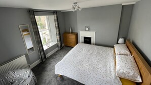 Une chambre à coucher avec un lit, une commode, un miroir, une cheminée et une fenêtre avec des rideaux.