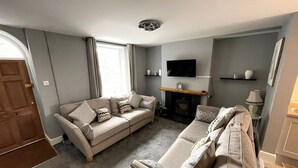 Un salon avec un ensemble de canapés de couleur beige, une cheminée, un téléviseur fixé au mur et une porte donnant sur une autre pièce.