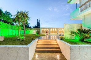 Een modern buitengebied met een betonnen trap naar een zwembad, omgeven door groen en een houten hek.