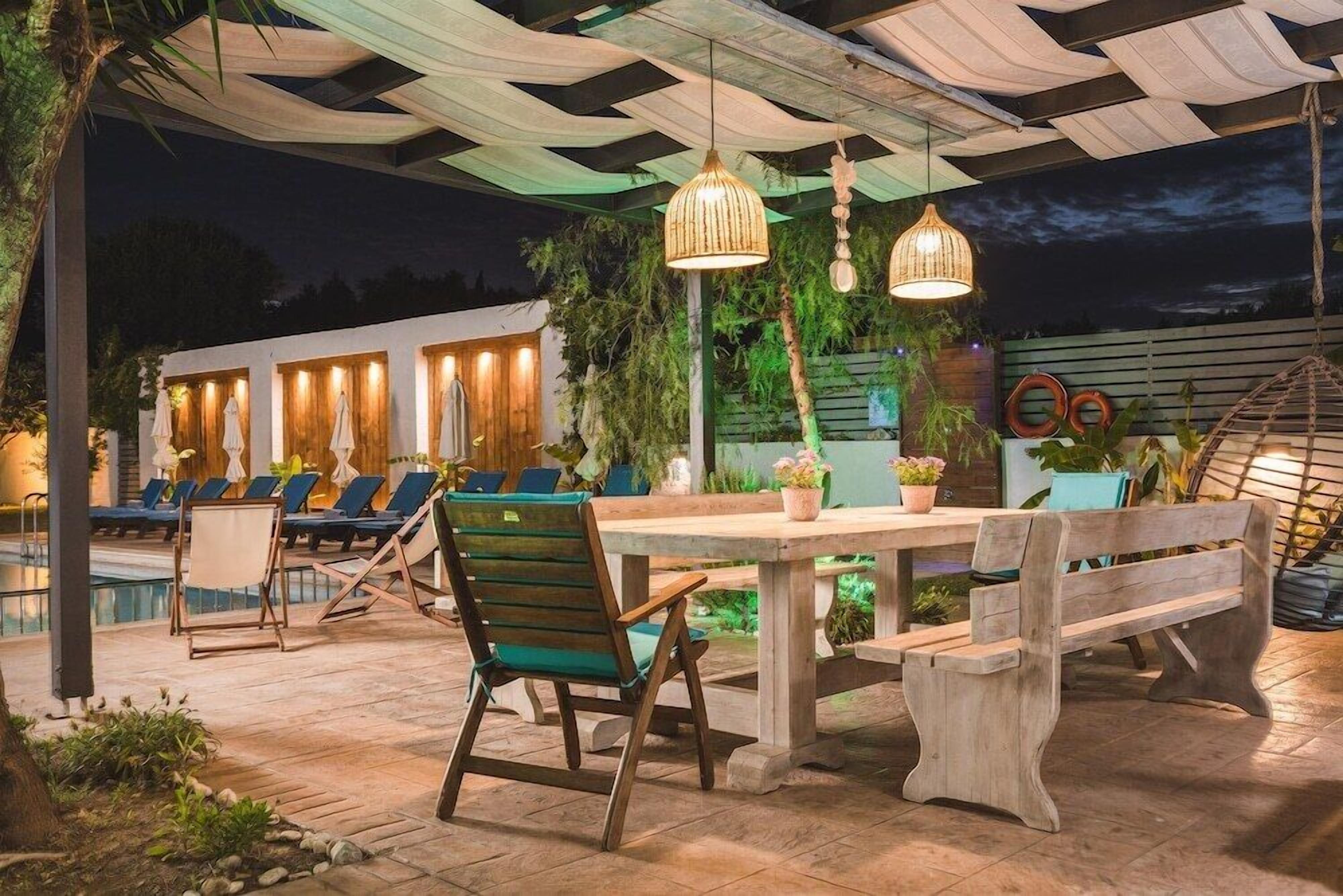 An outdoor patio with lounge chairs, a wooden table, and hanging pendant lights.
