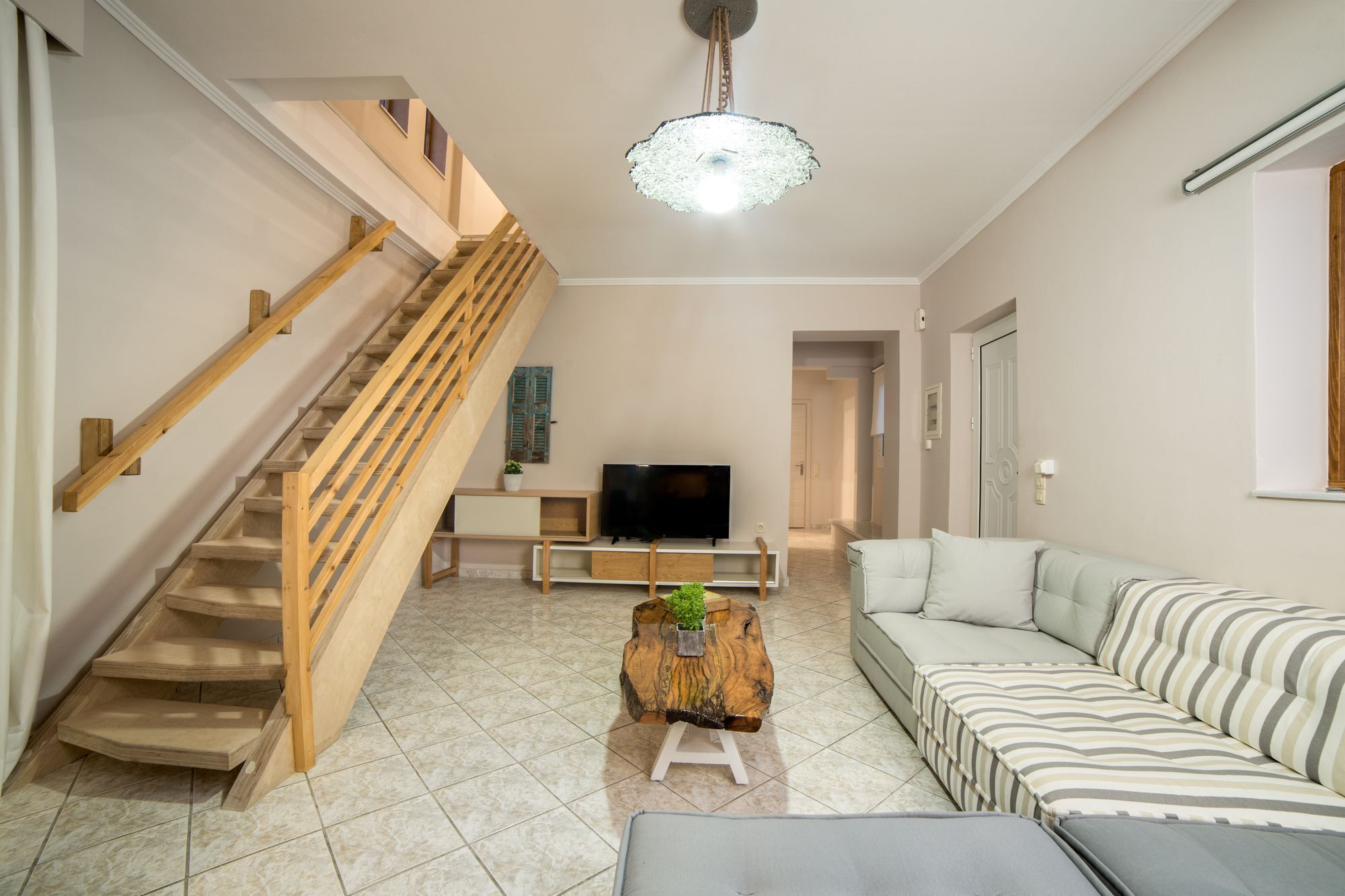 Un salon moderne avec un escalier en bois, un téléviseur à écran plat, un canapé et une table basse.