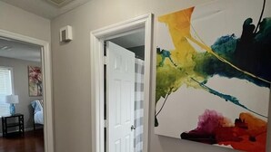 A hallway with wooden flooring, a white door, and a colorful abstract painting on the wall. - Executive Condo - Gigabit Wi-Fi - Near Redstone Arsenal - 2 beds-2 baths (Madison)