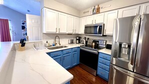 A modern kitchen with white and blue cabinets, stainless steel appliances, and a marble countertop. - Executive Condo - Gigabit Wi-Fi - Near Redstone Arsenal - 2 beds-2 baths (Madison)