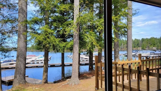 A view from a cabin overlooking a lake with docked boats, surrounded by tall trees. - Lakefront Muskoka Beautiful Cottage  (Gravenhurst)