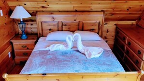 A wooden bed with a blue bedspread and two swan-shaped pillows in a cabin-style room with wooden walls and a wooden floor. - Lakefront Muskoka Beautiful Cottage  (Gravenhurst)