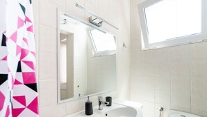 Une salle de bain avec un lavabo blanc, un miroir, des toilettes et une fenêtre.