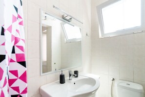 Une salle de bain avec un lavabo blanc, un miroir, des toilettes et une fenêtre.