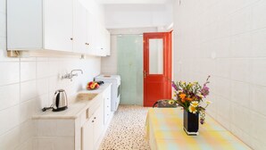Une cuisine compacte avec des meubles blancs, une bouilloire, un grille-pain et une petite table agrémentée d’un vase de fleurs.