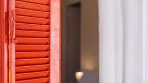 Une porte rouge à lattes horizontales, qui donne sur une pièce avec un mur blanc et une source de lumière visible à l’arrière-plan.