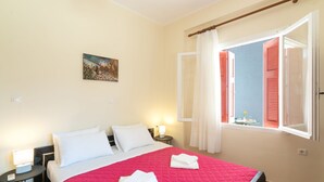Une chambre d’hôtel avec un lit, une table de chevet, une commode, une fenêtre avec des volets ouverts et un tableau au mur.