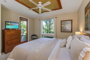 A bedroom with a bed, a wooden dresser, a television, and a ceiling fan.