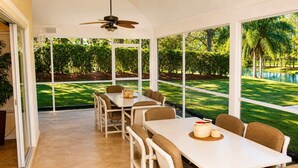 A dining area with a table and chairs, large windows, and a ceiling fan. - SWISS 24 - Lake Stephanie (Clermont)